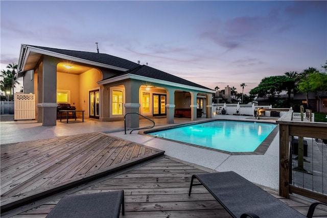 pool at dusk featuring fence, a deck, and a fenced in pool