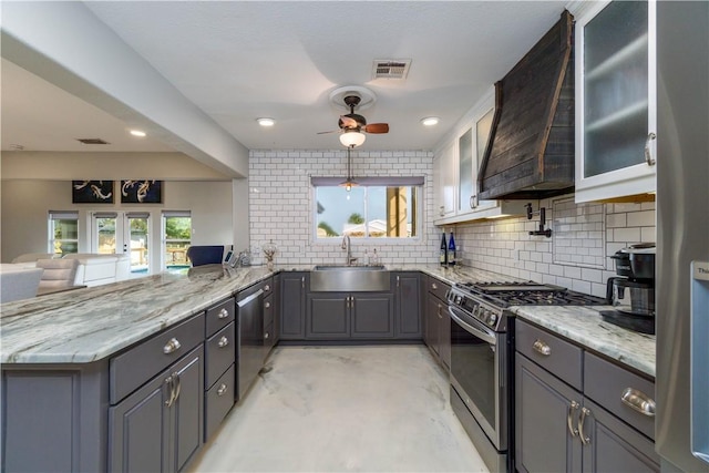 kitchen with light stone countertops, custom exhaust hood, stainless steel appliances, and a sink