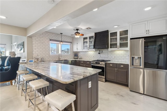 kitchen featuring wall chimney range hood, a kitchen breakfast bar, a peninsula, stainless steel appliances, and backsplash