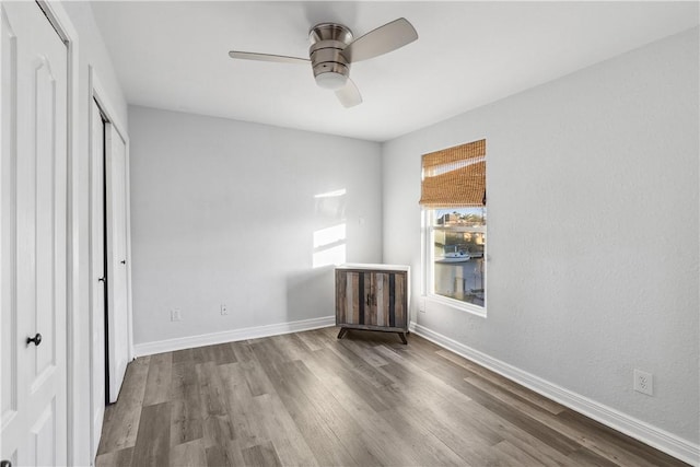 unfurnished bedroom with a closet, baseboards, a ceiling fan, and wood finished floors