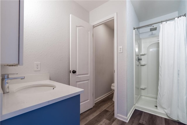 bathroom featuring toilet, a stall shower, wood finished floors, and a textured wall