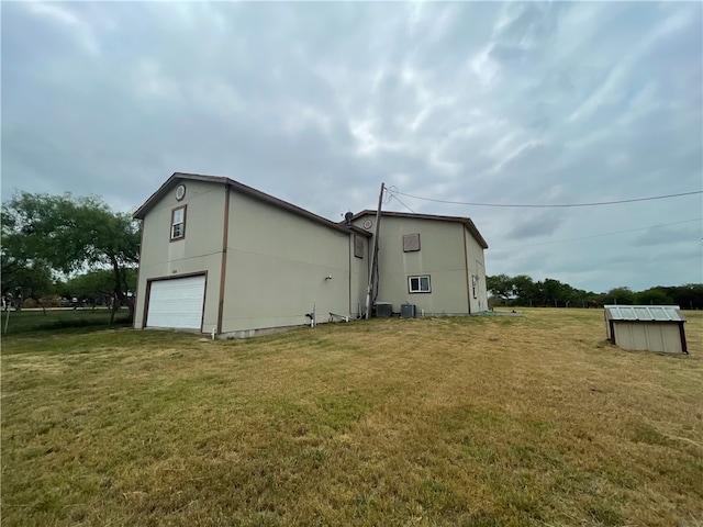 rear view of property with central air condition unit, a garage, and a yard