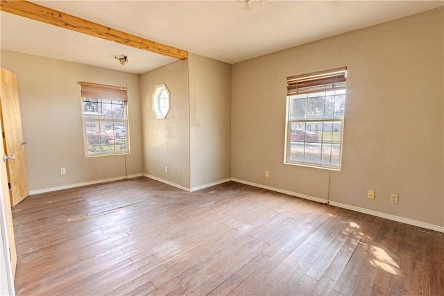 empty room featuring wood-type flooring, a healthy amount of sunlight, and beam ceiling