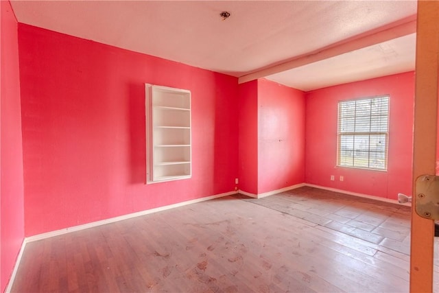 spare room with hardwood / wood-style floors and beam ceiling