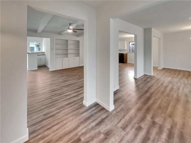 unfurnished living room with a ceiling fan, beamed ceiling, baseboards, and wood finished floors