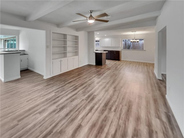 unfurnished living room with light wood-style floors, baseboards, beam ceiling, and ceiling fan with notable chandelier