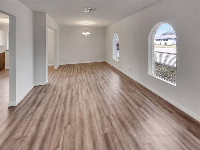 spare room featuring baseboards, visible vents, a notable chandelier, and light wood finished floors