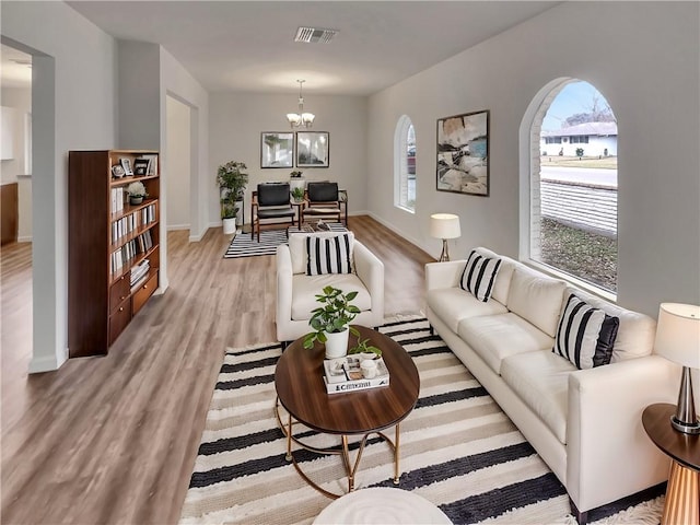 living area featuring baseboards, light wood-type flooring, visible vents, and a notable chandelier