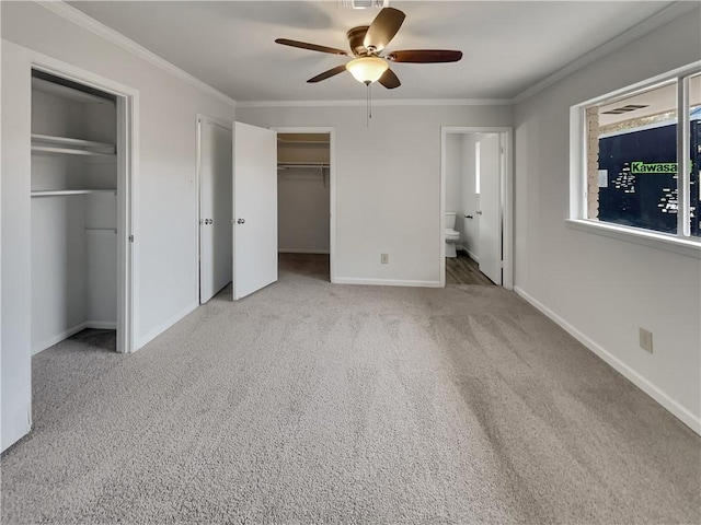 unfurnished bedroom with baseboards, ornamental molding, ensuite bathroom, carpet, and two closets