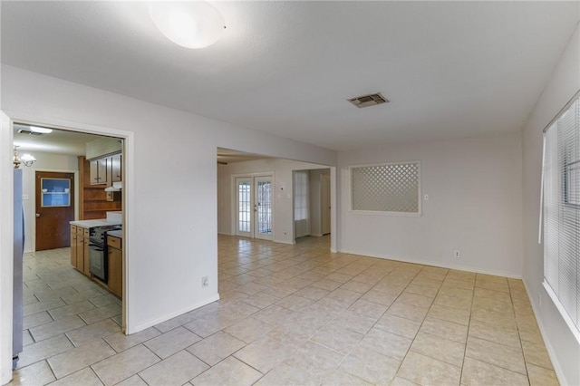 tiled empty room with an inviting chandelier and french doors