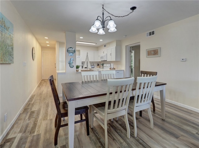 dining room with light wood-type flooring and an inviting chandelier