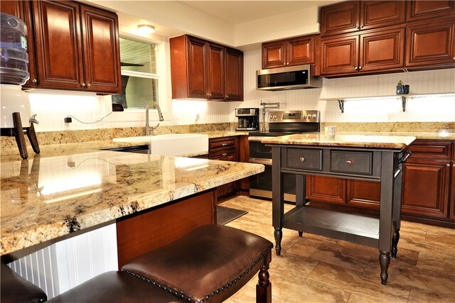 kitchen featuring stainless steel appliances, sink, a breakfast bar area, and light stone countertops