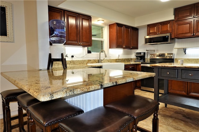 kitchen with sink, kitchen peninsula, appliances with stainless steel finishes, light stone countertops, and a breakfast bar area