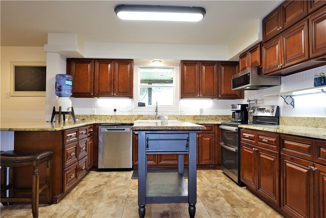 kitchen featuring stainless steel appliances, sink, light stone counters, and a breakfast bar