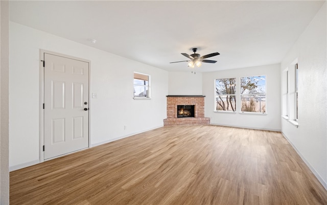 unfurnished living room featuring light wood-type flooring, ceiling fan, a brick fireplace, and a wealth of natural light