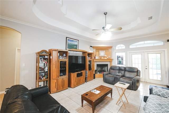 living room with light tile patterned flooring, ceiling fan, a raised ceiling, and ornamental molding