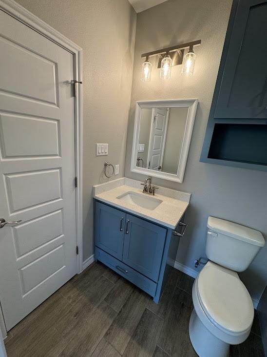 bathroom featuring baseboards, wood finished floors, toilet, and vanity