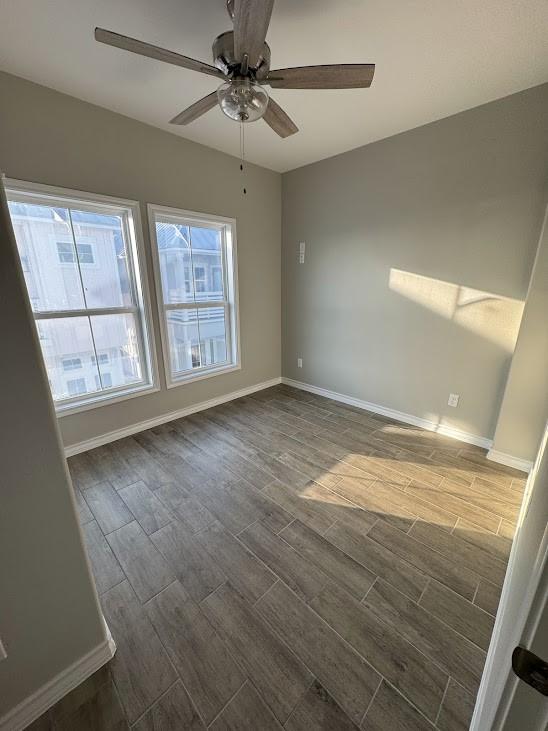 empty room with baseboards, wood finish floors, and a ceiling fan