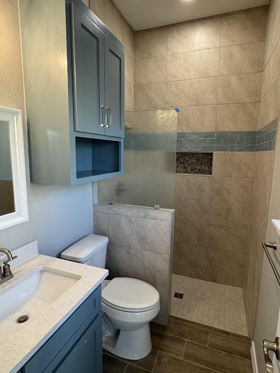full bath with toilet, a walk in shower, vanity, and wood finish floors