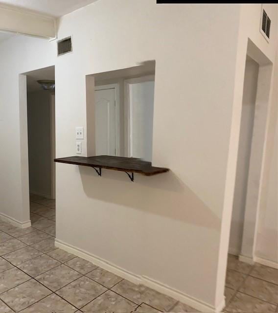 corridor with light tile patterned floors, visible vents, and baseboards