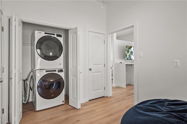 laundry room with stacked washing maching and dryer and light hardwood / wood-style flooring