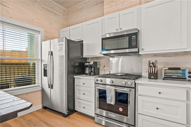 kitchen with light hardwood / wood-style flooring, appliances with stainless steel finishes, tasteful backsplash, white cabinets, and wood walls