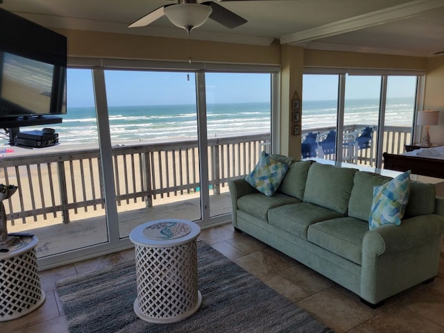 living room featuring a view of the beach, a water view, ornamental molding, ceiling fan, and tile patterned floors