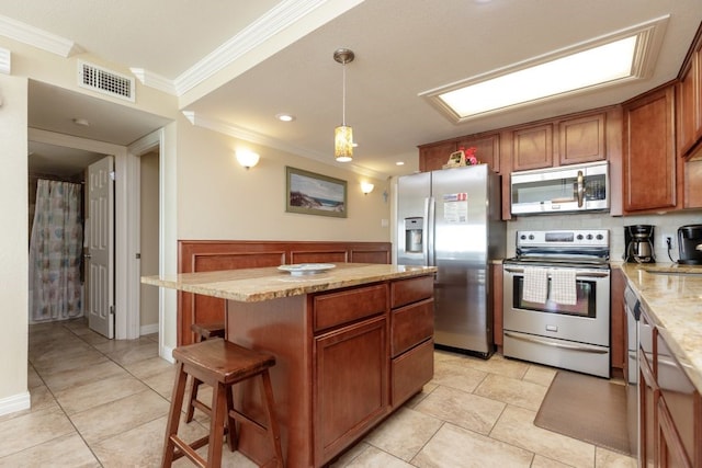 kitchen featuring crown molding, appliances with stainless steel finishes, a kitchen bar, pendant lighting, and a center island