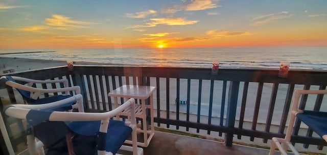 balcony at dusk featuring a view of the beach and a water view