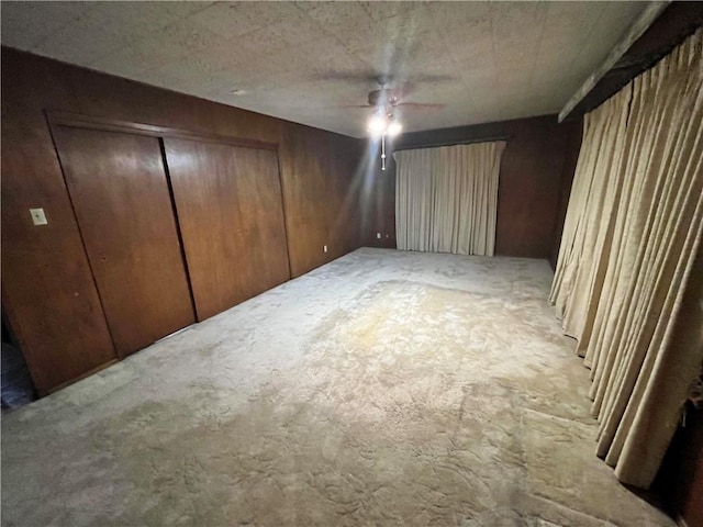 unfurnished bedroom with light carpet, a closet, ceiling fan, and wood walls