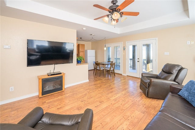 living room featuring ceiling fan, light hardwood / wood-style floors, a raised ceiling, and french doors