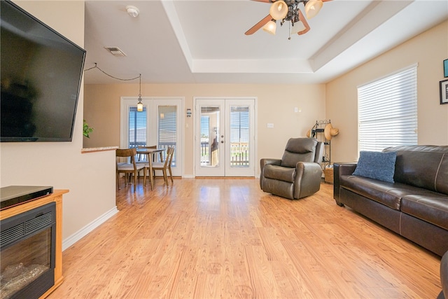 living room with ceiling fan, french doors, a tray ceiling, and light hardwood / wood-style flooring