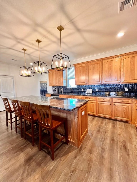 kitchen with ornamental molding, light wood-type flooring, decorative light fixtures, dark stone countertops, and a center island