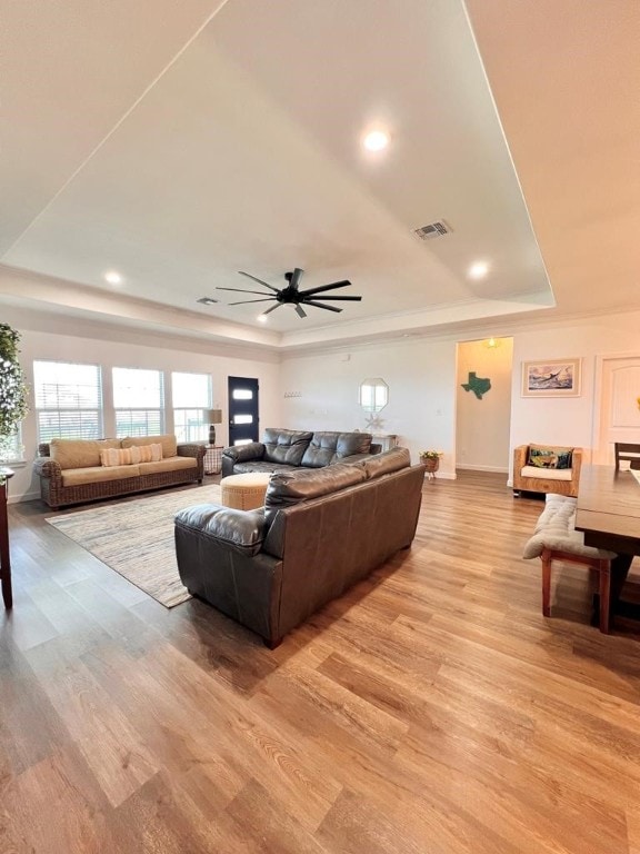 living room featuring light wood-type flooring, a tray ceiling, and ceiling fan