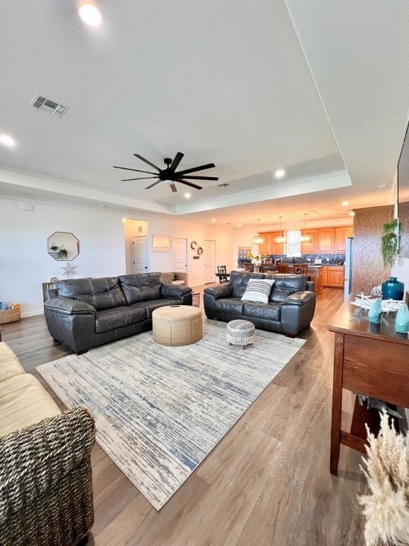 living room with a tray ceiling, hardwood / wood-style floors, and ceiling fan