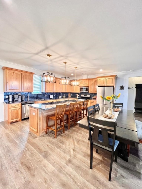 kitchen with stainless steel appliances, backsplash, light hardwood / wood-style flooring, a kitchen island, and pendant lighting