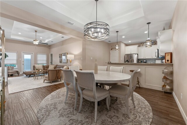 dining space with ceiling fan with notable chandelier, dark hardwood / wood-style floors, and a raised ceiling