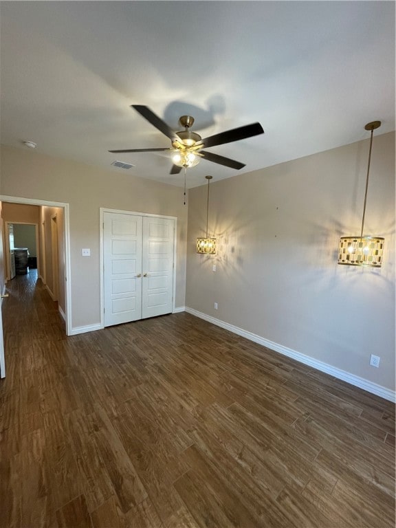 unfurnished bedroom with ceiling fan with notable chandelier, dark wood-type flooring, and a closet