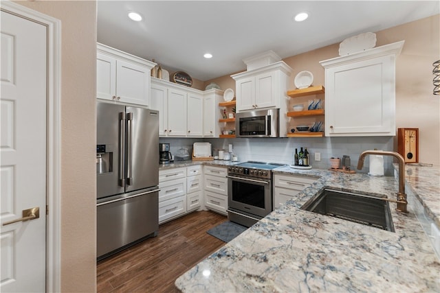 kitchen with stainless steel appliances, white cabinetry, sink, light stone counters, and dark hardwood / wood-style floors