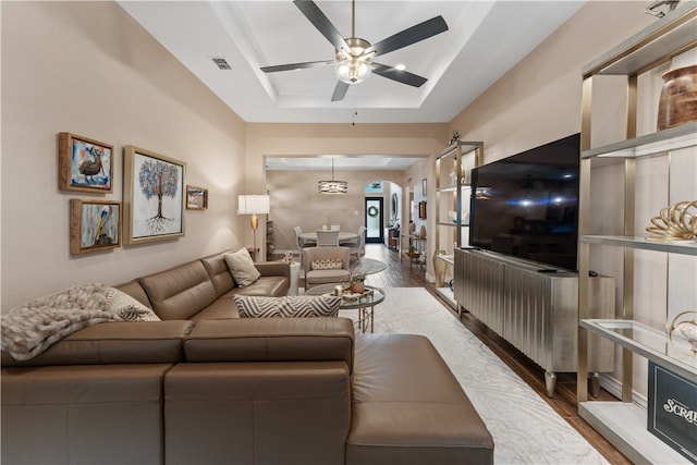 living room featuring wood-type flooring, ceiling fan, and a raised ceiling