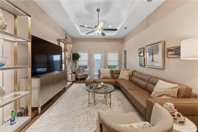 living room with ceiling fan, wood-type flooring, and a tray ceiling