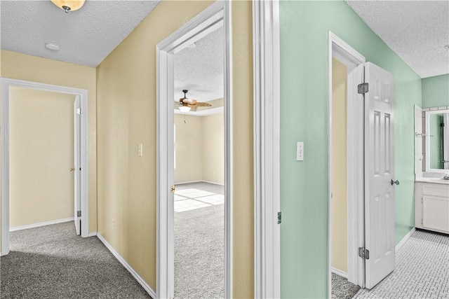 hallway with baseboards, carpet flooring, and a textured ceiling