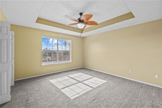 empty room featuring a textured ceiling, baseboards, carpet, ceiling fan, and a raised ceiling