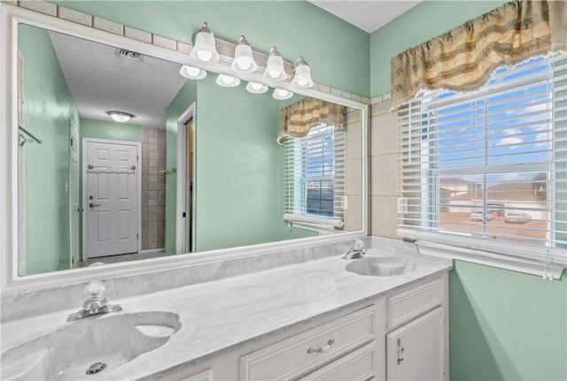 bathroom with a textured ceiling, a sink, visible vents, and double vanity