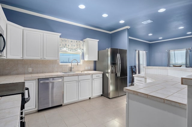 kitchen with sink, a wealth of natural light, appliances with stainless steel finishes, tile counters, and white cabinetry