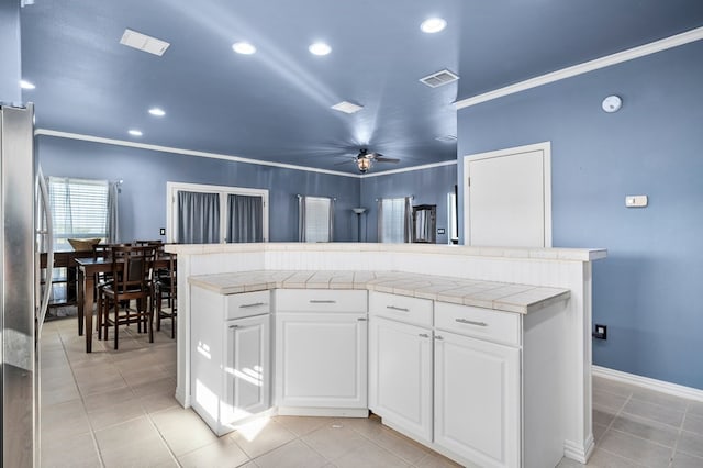 kitchen featuring tile countertops, white cabinets, ceiling fan, light tile patterned flooring, and stainless steel refrigerator