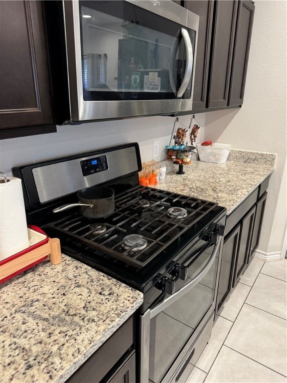 kitchen featuring dark brown cabinetry, light tile patterned flooring, light stone countertops, and appliances with stainless steel finishes