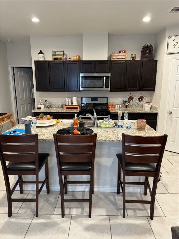 kitchen featuring stainless steel appliances, a center island with sink, a breakfast bar, and light stone counters