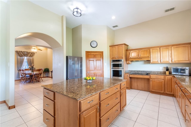 kitchen with a high ceiling, light tile patterned floors, appliances with stainless steel finishes, and a center island