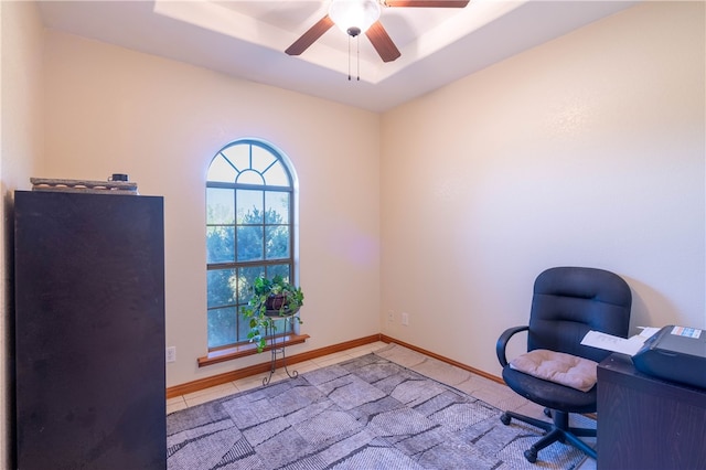 unfurnished office with ceiling fan, a tray ceiling, and light tile patterned flooring